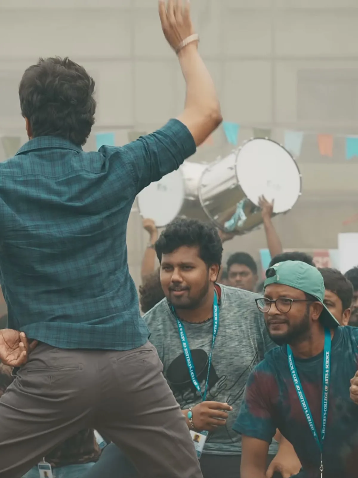 Vijay — From behind — the shirt worn loose over the taupe chinos, and the pale band on his right wrist
