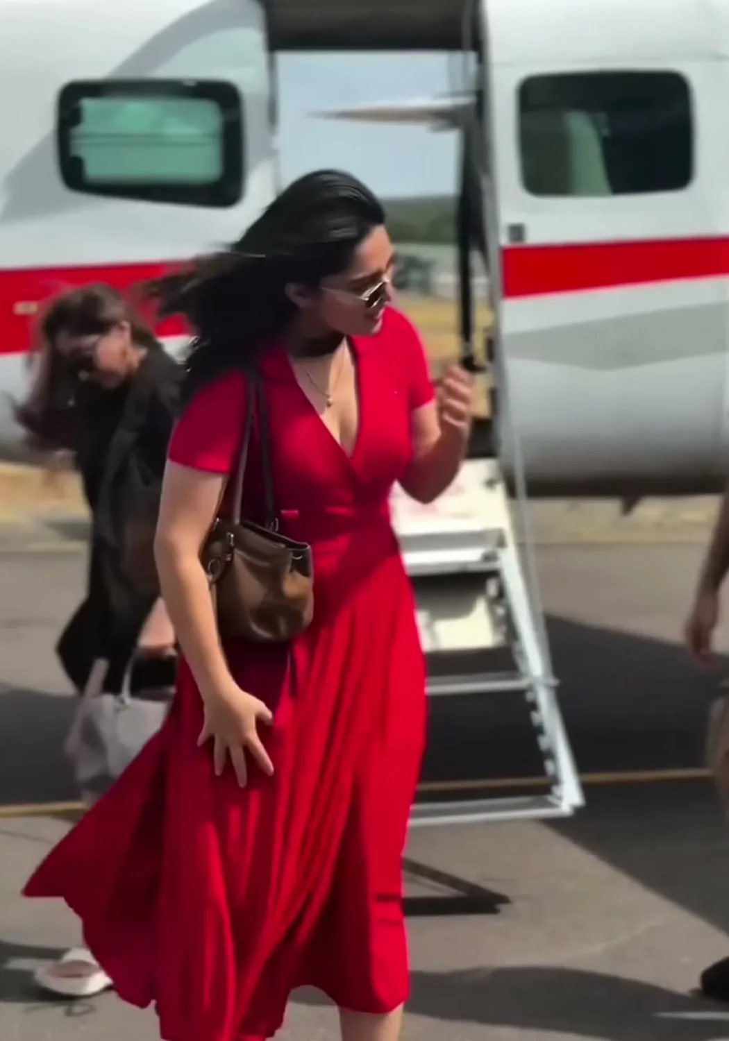 Kayadu Lohar — The whole outfit — red wrap dress, tan shoulder bag, dark glasses, and nothing else