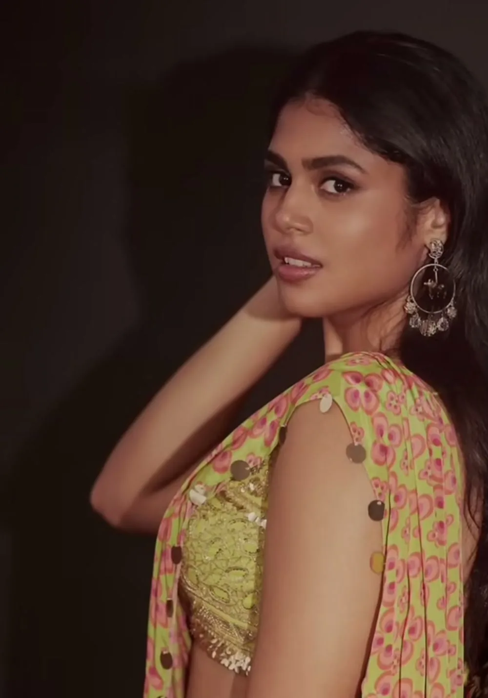 Faria Abdullah — Turned three-quarters — the oxidised hoops and the scalloped, bobble-trimmed edge of the pallu